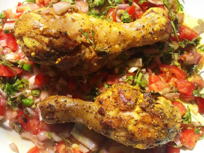 Spice-coated chicken on a bed of tomato onion salad garnished with lemon