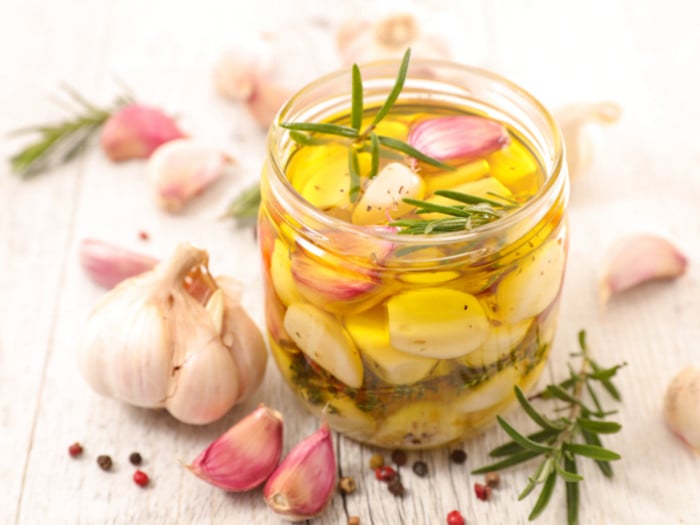 A mini jar of garlic infused olive oil with dill, garlic pods, and a whole garlic