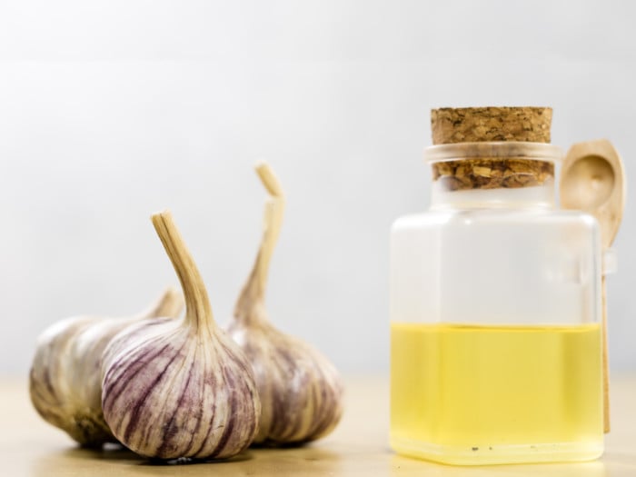 A jar of garlic juice with whole garlic on a wooden table