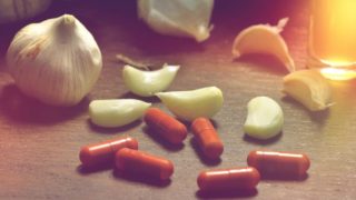 Garlic pods and pills on a wooden surface