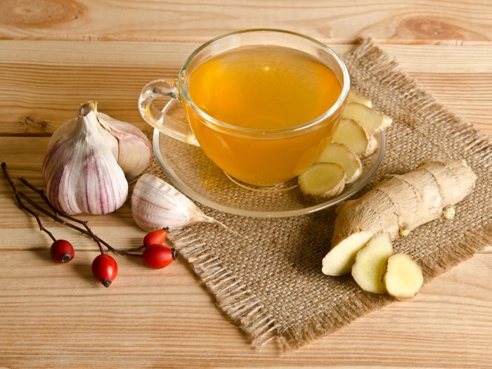 A cup of garlic ginger tea, red cherries, halved and sliced garlic and ginger on a wooden table