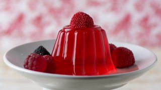 A white plate of raspberry jelly with raspberries on top and next to the jelly