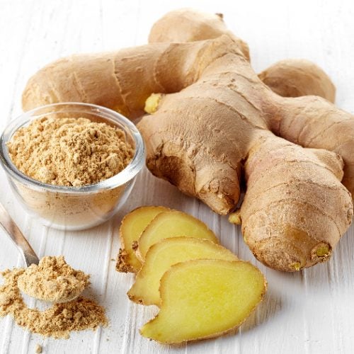 Ginger powder in a bowl and a couple of ginger pieces around