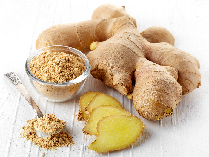 Ginger powder in a bowl and a couple of ginger pieces around