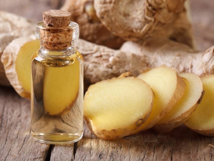 A container of ginger essential oil with sliced and whole ginger on a wooden table