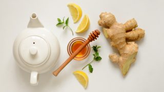 Flatlay picture of a white kettle, honey, lemon, ginger, and mint leaves