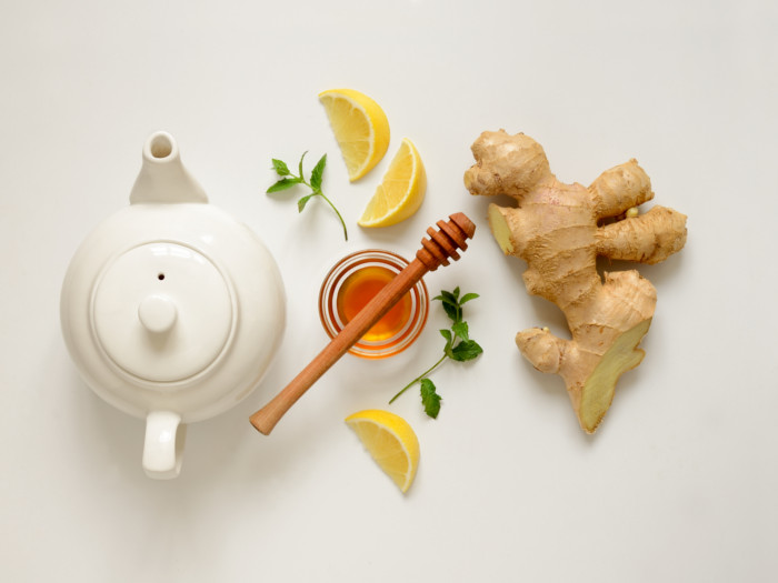 Flatlay picture of a white kettle, honey, lemon, ginger, and mint leaves