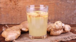 A glass of ginger juice, surrounded by ginger, kept atop a wooden table