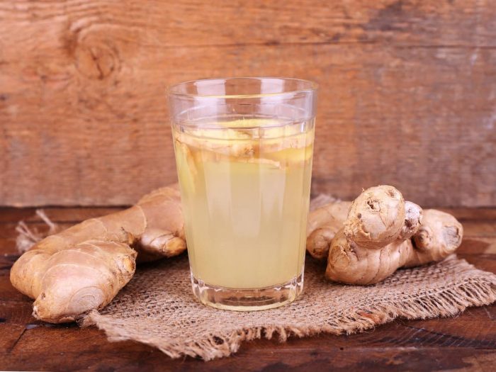 A glass of ginger juice, surrounded by ginger, kept atop a wooden table