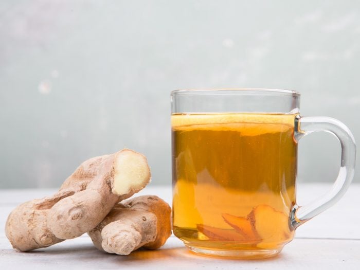 A cup of ginger root tea with halved gingers on a white background