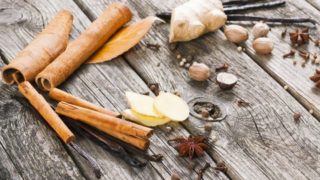 Whole spices like ginger root, sliced ginger, vanilla beans, star anise, and cinnamon sticks on wood