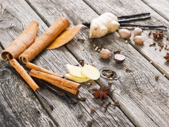 Whole spices like ginger root, sliced ginger, vanilla beans, star anise, and cinnamon sticks on wood