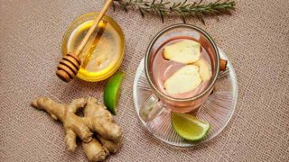 A cup of ginger tea with sliced lemon, a bowl of honey, and ginger on burlap