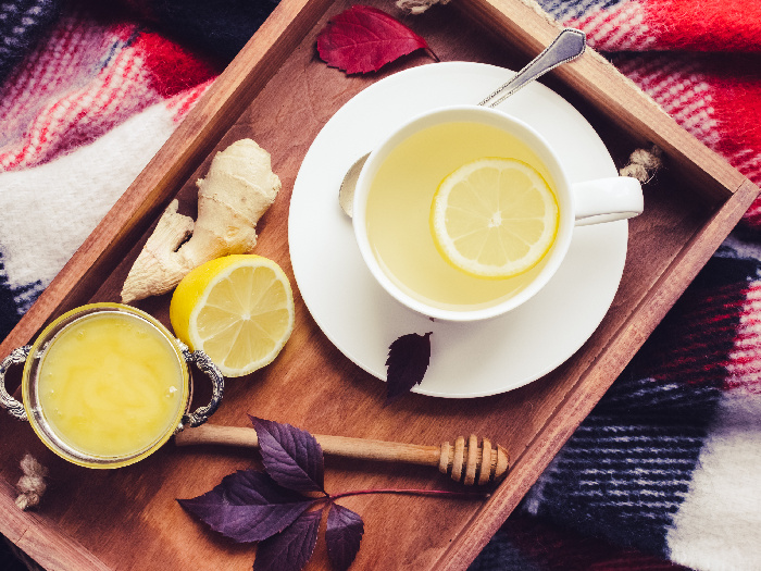 Ginger tea with honey, ginger root and lemon on a wooden tray on a red warm woolen blanket