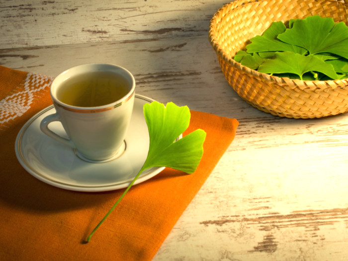 A cup of ginkgo biloba tea next to a basket filled with fresh ginkgo biloba leaves