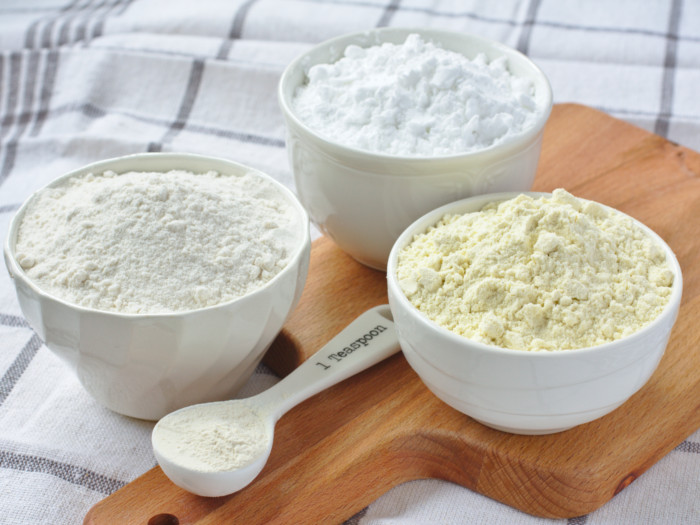 Three white bowls and a teaspoon of flour on a wooden board, placed on a check cloth