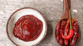 Gochujang paste in a small white dish with fresh and dried chilies next to it