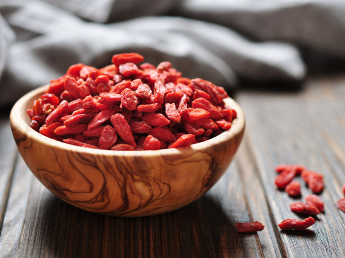 A bowl of goji berries in a wooden bowl placed on a wooden surface.