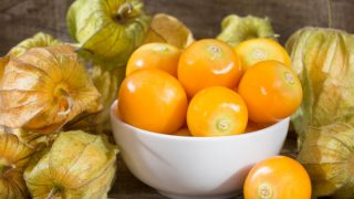A white bowl of fresh golden berries and berries on a wooden table