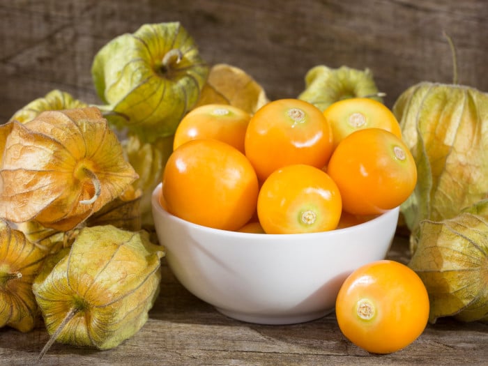 Una ciotola bianca di bacche d'oro fresche e frutti di bosco su un tavolo di legno