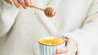 Healthy vegan turmeric latte or golden milk with honey in female hands