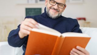 Middle-aged man wearing glasses and reading a book with a smile
