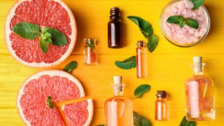 Bottles of grapefruit essential oil, slices of grapefruit and a bowl of sea salt on a yellow background