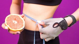 A grapefruit in one hand while measuring the waist with the other