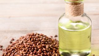 A glass bottle of grapeseed oil with grape seeds next to it