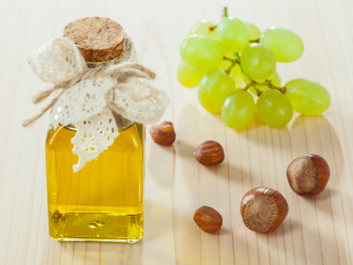 A bottle of grapeseed oil with a bunch of grapes and nuts on the side