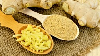 Ginger roots placed alongside two spoons containing grated and powdered ginger on a burlap cloth.