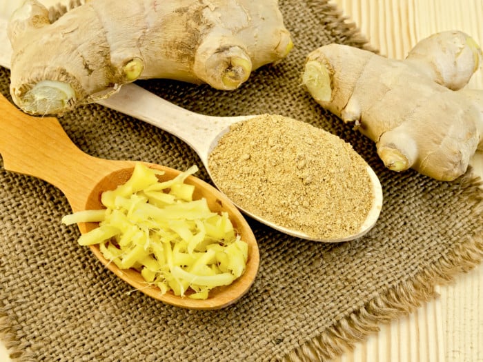 Ginger roots placed alongside two spoons containing grated and powdered ginger on a burlap cloth.