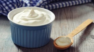 Yogurt in a blue bowl and wooden spoon with yogurt lying next to it