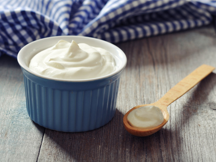 Yogurt in a blue bowl and wooden spoon with yogurt lying next to it