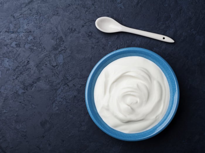 Top view of yogurt in a blue bowl and a spoon lying next to it