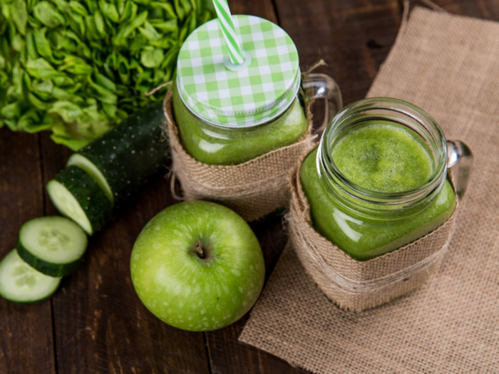 Green smoothies in a jar next to a green apple and cucumber