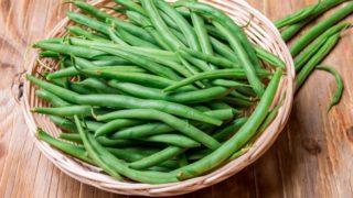 A basket filled with fresh green beans placed on a wooden table
