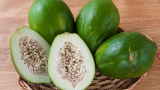 A basket of fresh whole and halved unripe papayas on a wooden table