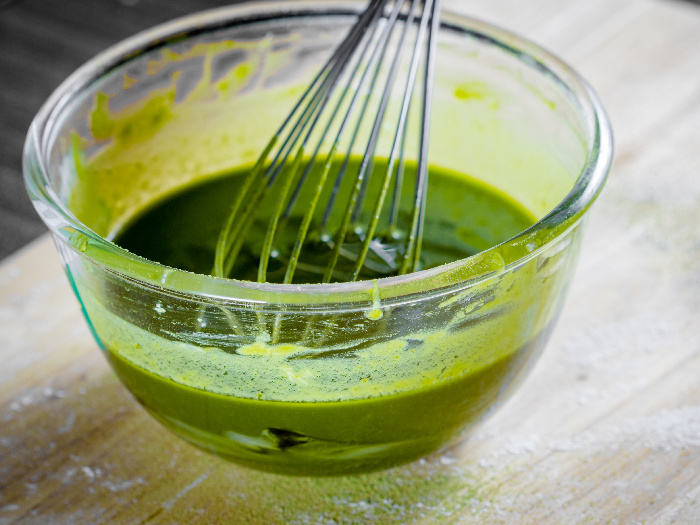 Mixing eggs, flour, and green tea in a bowl with a whisk to make a green tea cake