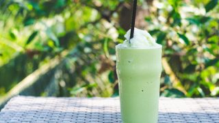 A glass of green tea frappe ice shake with a green plant background