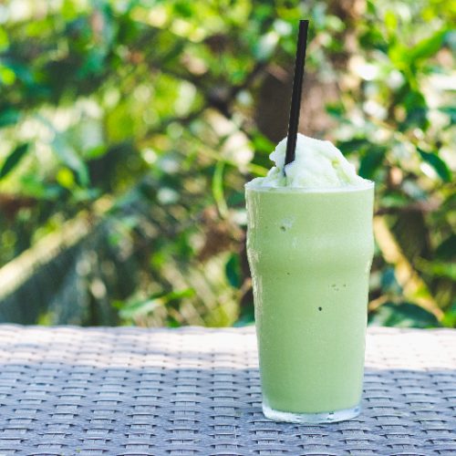 A glass of green tea frappe ice shake with a green plant background