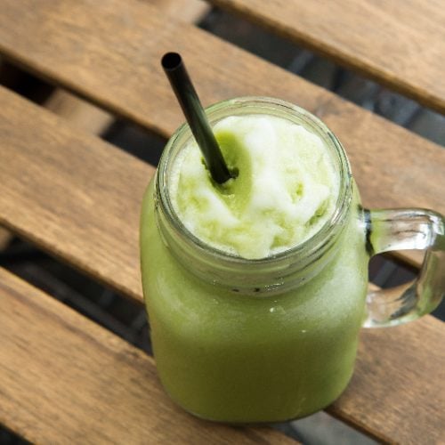 Green tea matcha smoothie with black straw in a glass cup on wood table