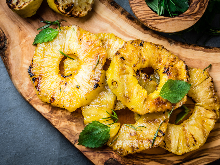 Grilled pineapple slices with fresh mint on a wooden cutting board