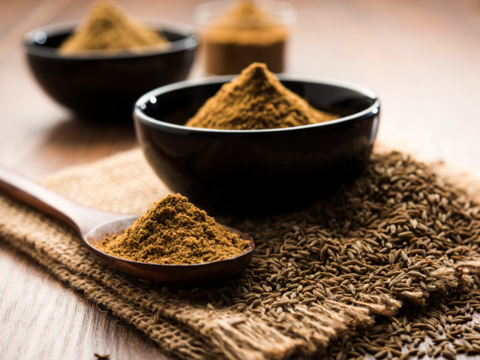 Ground cumin in a spoon and bowl placed on a burlap