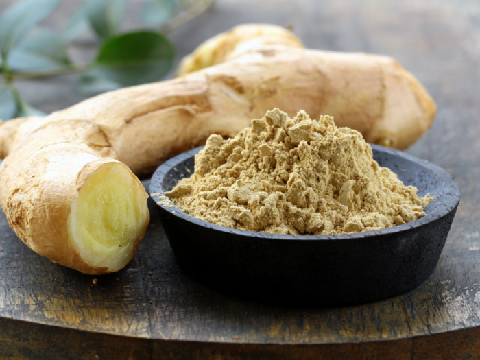 Ground ginger powder in a black bowl with a piece of ginger alongside it.