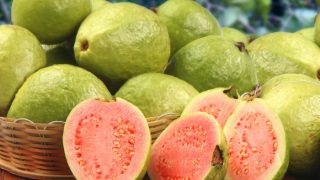 A basket of fresh and ripe guavas with sliced guavas on a wooden table
