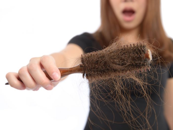 A woman looking upset with hair loss as she holds a comb with hair strands