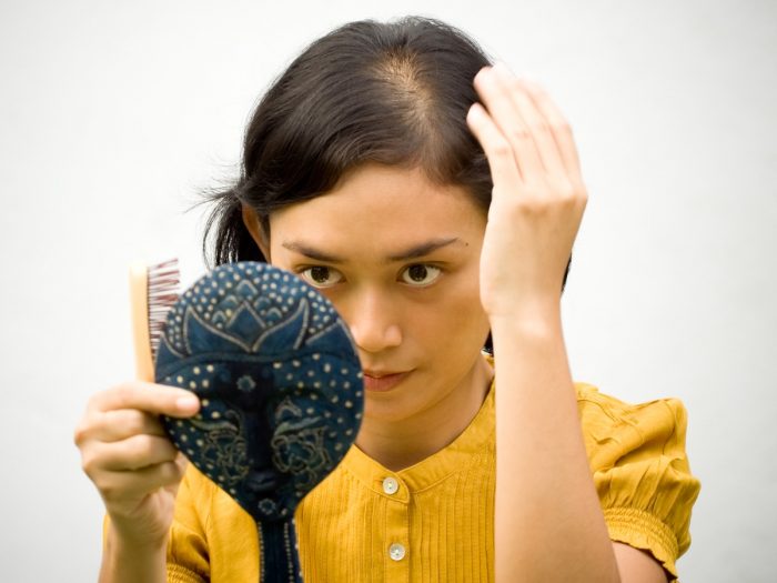 A woman with a hairbrush and ornamental mirror, looking at a bald patch