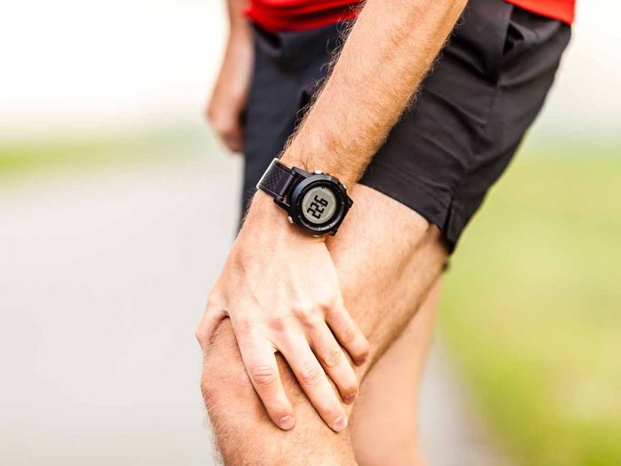 A man in running clothes wearing a digital watch, holding his knee