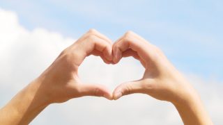 Hands in the form of heart on blue sky background
